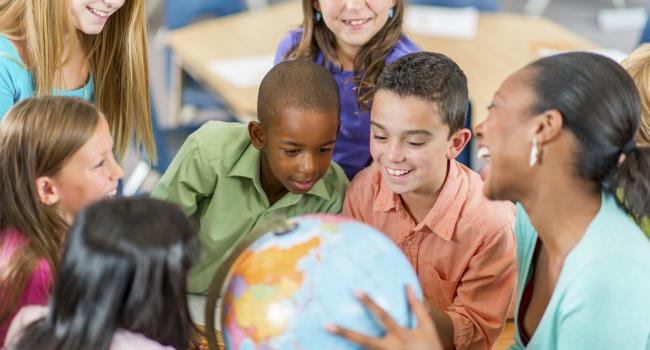 A teacher and students look at a globe