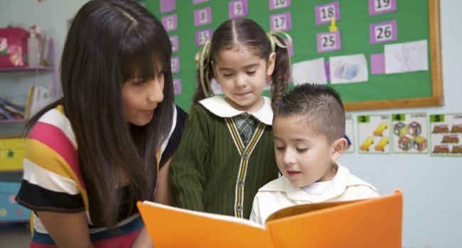 a woman looking at a book with two children. the boy is reading.